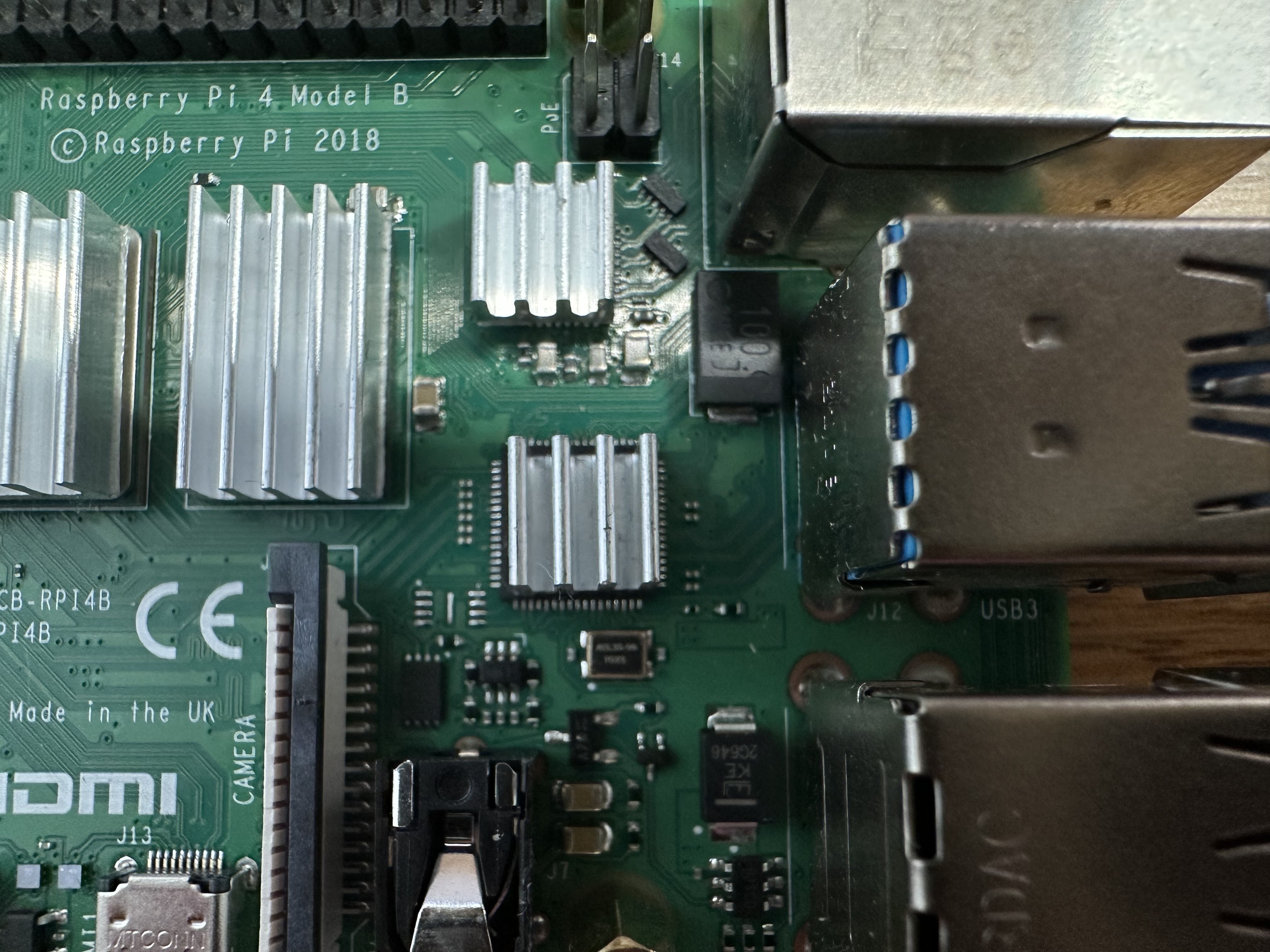 Close-up of the Raspberry Pi 4 board showing three stick-on silver heatsinks over the main chips, with the 'Raspberry Pi 4 Model B 2018' silkscreen visible beside them.