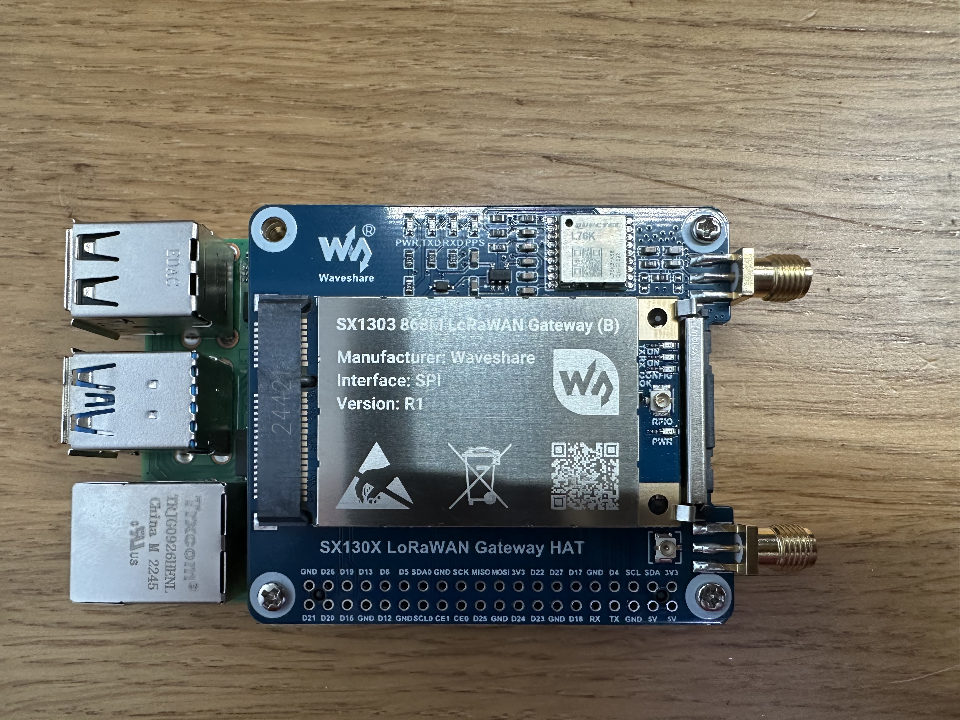 Top-down view of the Waveshare HAT on the Pi, with the silver-shielded SX1303 concentrator module seated in the mini-PCIe socket, labelled 'SX1303 868M LoRaWAN Gateway (B), Interface: SPI, Version: R1', and the small square L76K GPS module to its right.